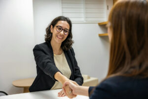 Two women shaking hands during a job interview in an office setting.