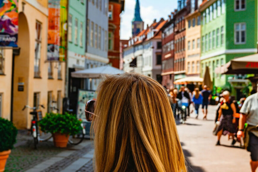 A woman walking through a colourful street in Denmark, with people, bicycles, and historic buildings in the background.