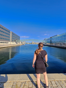Szilvia standing by the water in Copenhagen, looking across the harbour while reflecting on rebuilding her career in Denmark.